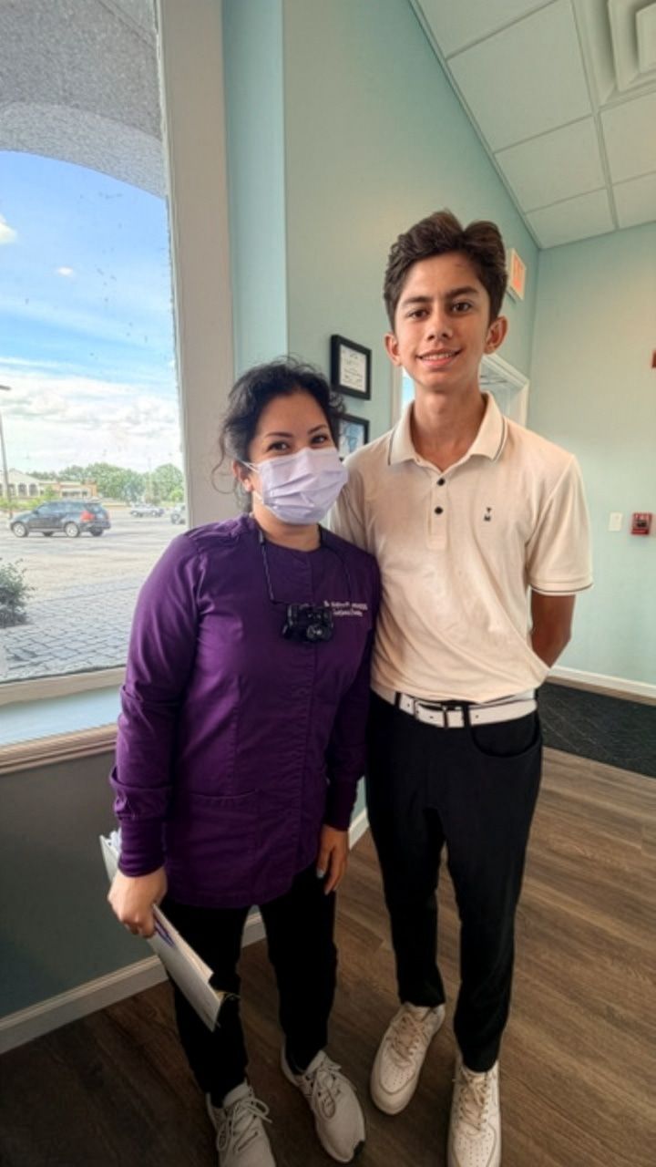 Orion standing beside a dentist in a mask and purple scrubs in a dental office.